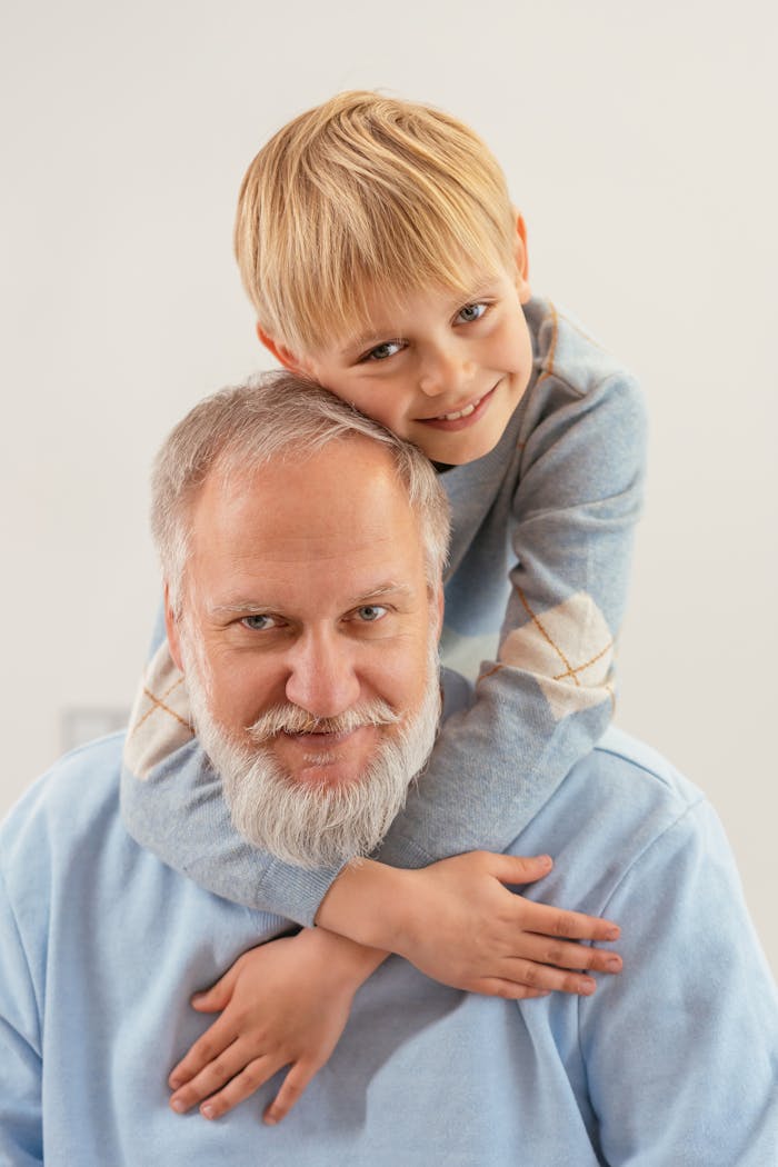 Portrait of a happy grandfather and grandson embracing indoors with a white background.