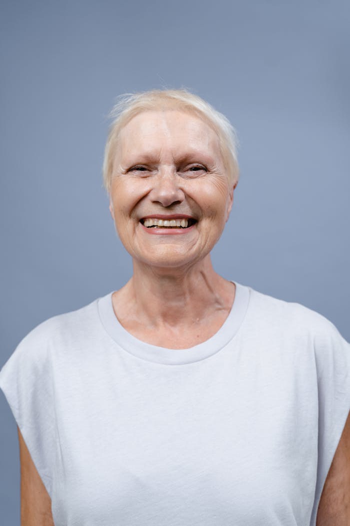 Radiant elderly woman smiling warmly against a neutral background.